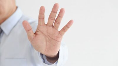 Close-up of a hand raised in a stop gesture against a white background to represent menghentikan pertengkaran.
