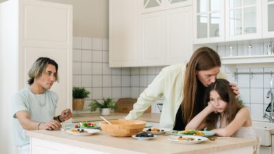 Seorang anak terlihat sedih sedang ditenangkan orang tuanya di dapur sebagai ilustrasi dampak parentification.