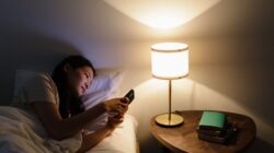 Seseorang memegang smartphone di tempat tidur saat bangun pagi.