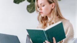 Seseorang sedang membaca buku di era digital dengan latar belakang perangkat teknologi.