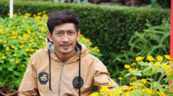 Pria dewasa tersenyum percaya diri dengan latar belakang modern, merepresentasikan karisma dan daya tarik.