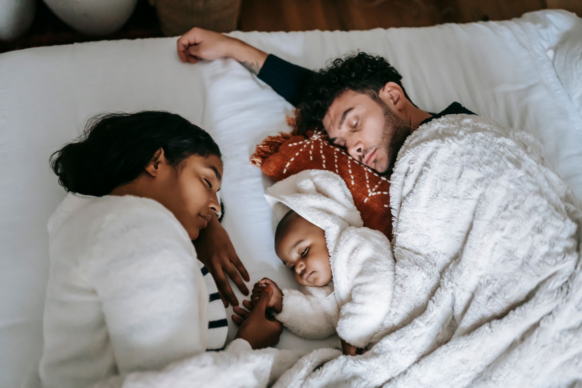 Seorang bayi tidur di tempat tidur dewasa, menggambarkan risiko bahaya bayi tidur bersama orang tua.
