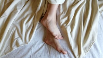 Seseorang memegang kaki yang terasa sakit saat bangun tidur di atas tempat tidur putih.