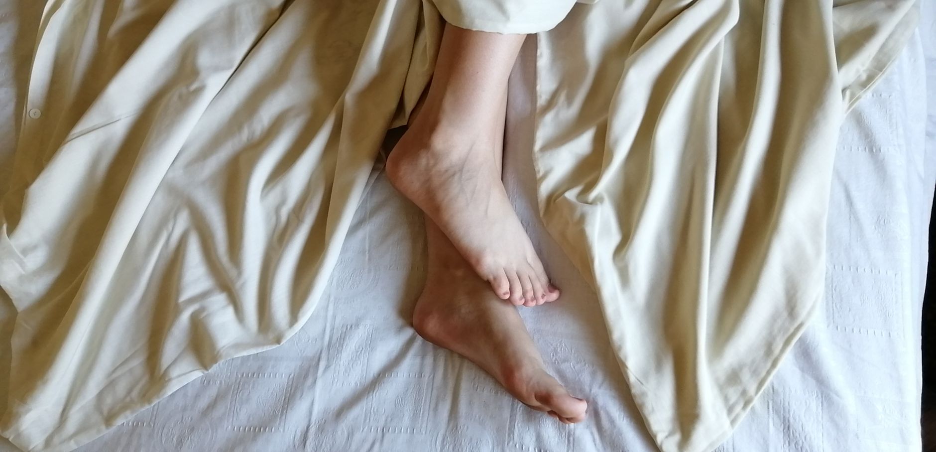 Seseorang memegang kaki yang terasa sakit saat bangun tidur di atas tempat tidur putih.