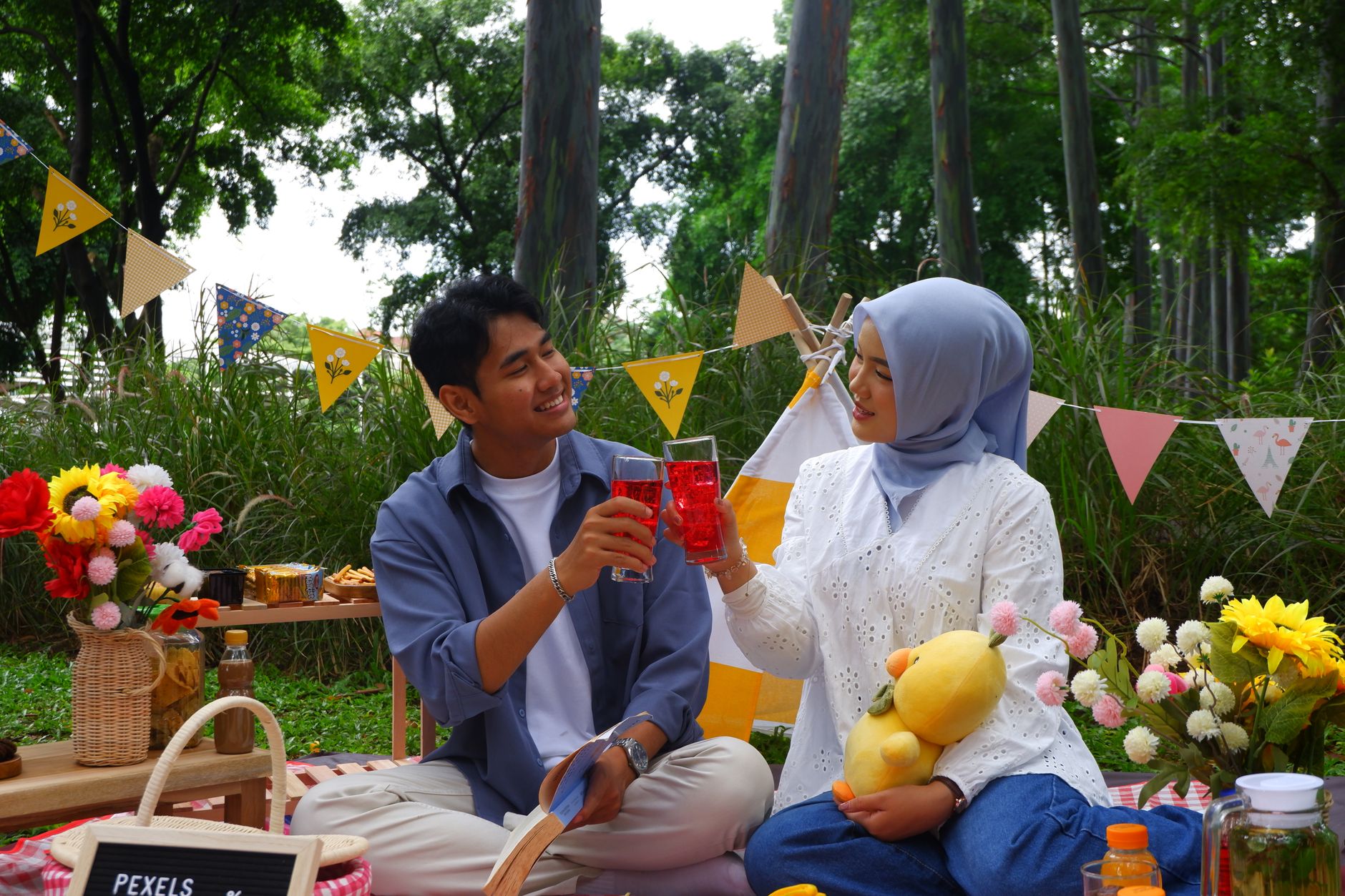 A young Muslim couple clinks glasses during a picnic in a park while memulai kencan kembali.