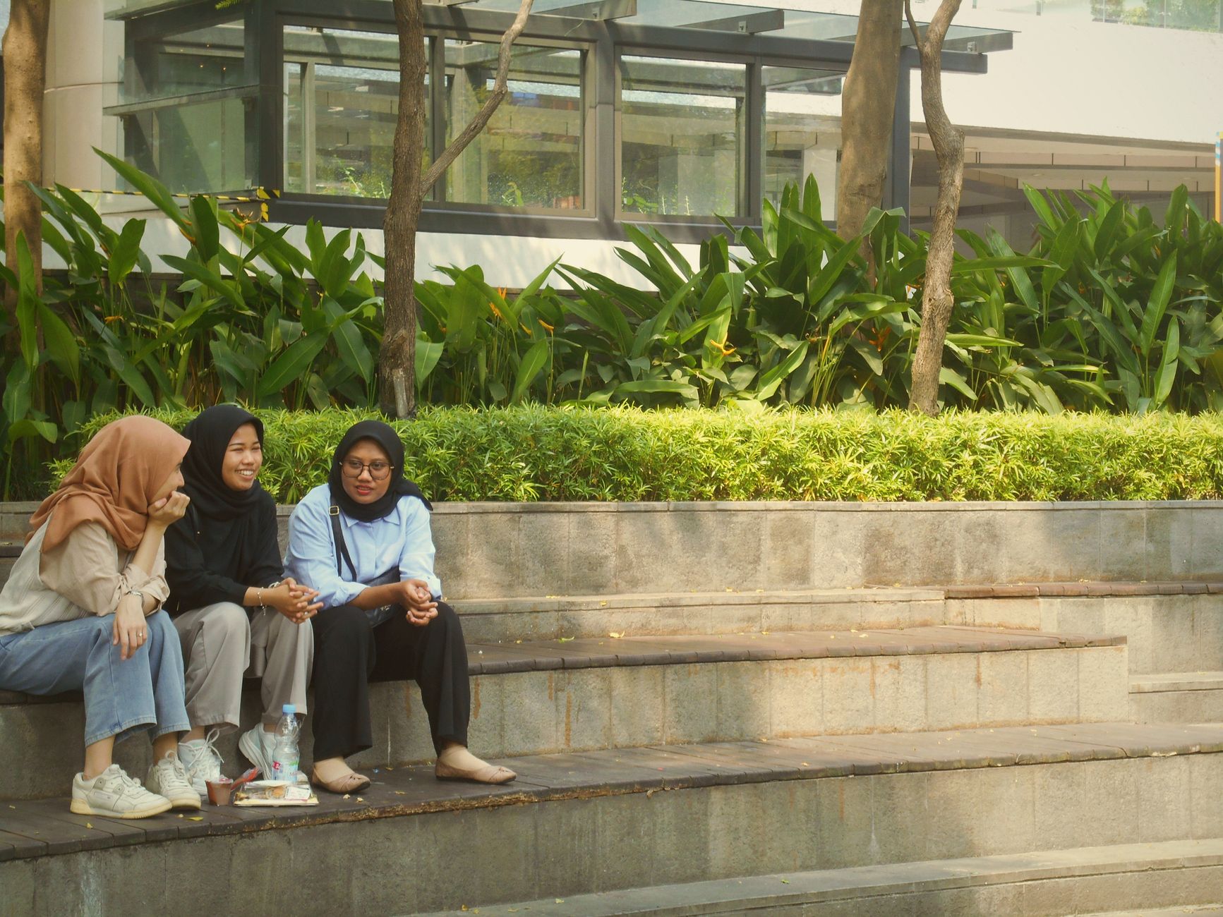 Tiga wanita berhijab duduk di tangga luar ruangan sambil mengobrol, terkait persepsi waktu santai.