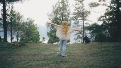 A woman in a hijab with arms outstretched, enjoying scenic forest views for hidup bahagia.
