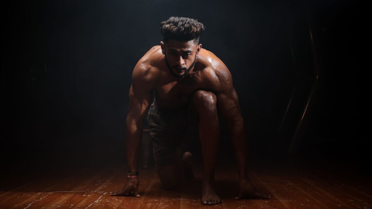 Athletic sprinter in a ready position on a wooden floor, representing ways of memulihkan stamina tubuh.