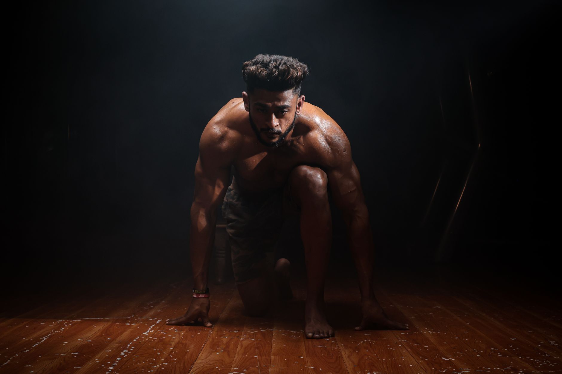 Athletic sprinter in a ready position on a wooden floor, representing ways of memulihkan stamina tubuh.