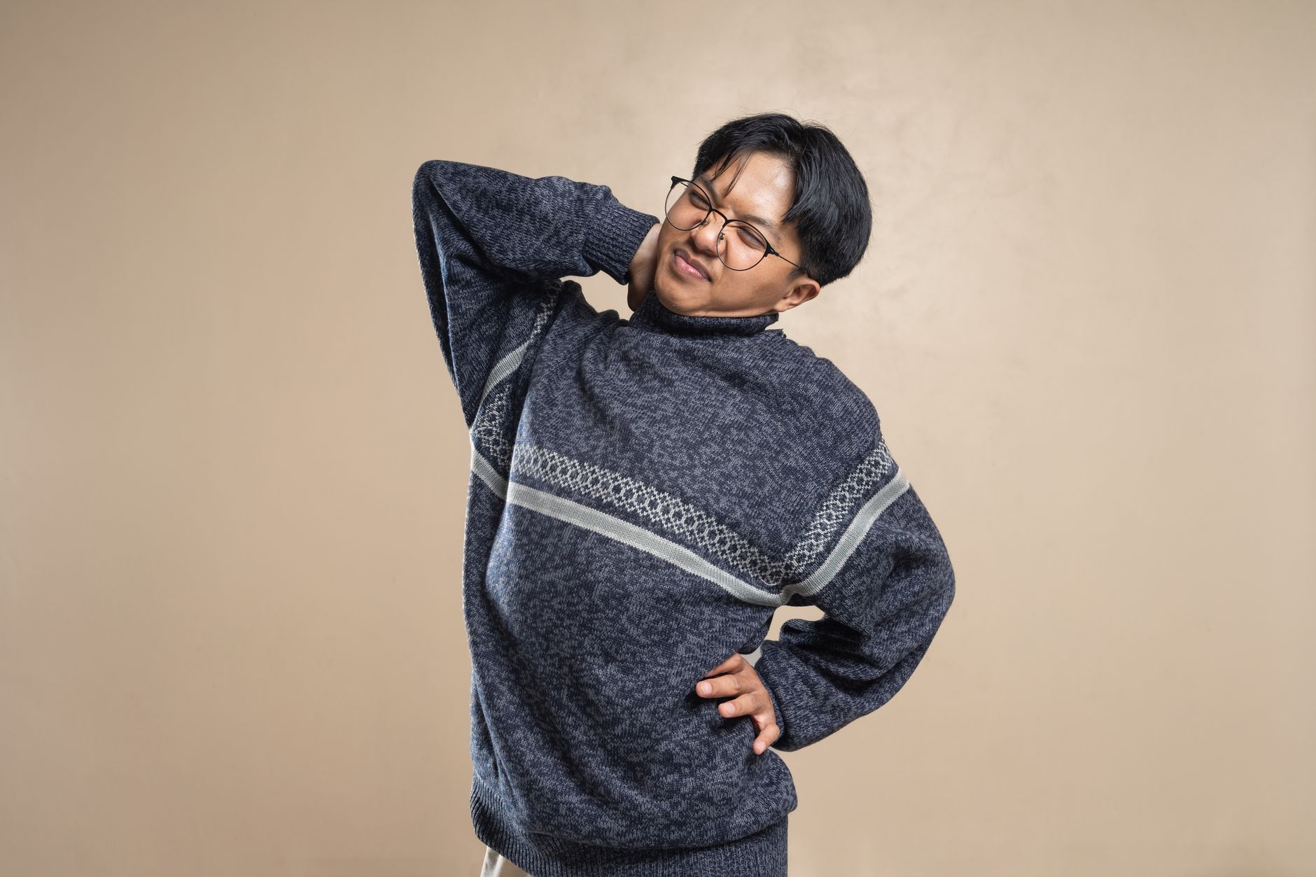 Seorang pria ber sweater abu-abu memegang lehernya karena nyeri saat mengalami tegang saraf.