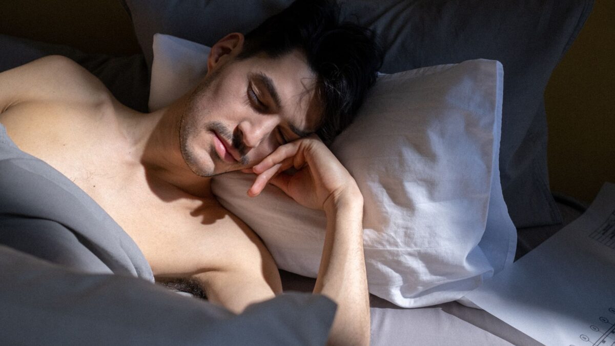 A young man sleeping peacefully in bed with morning sunlight streaming in.
