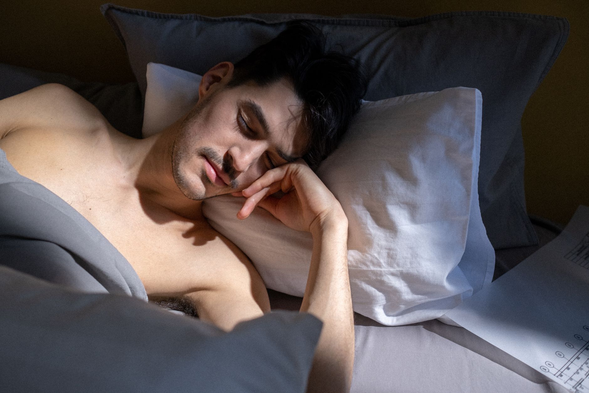 A young man sleeping peacefully in bed with morning sunlight streaming in.