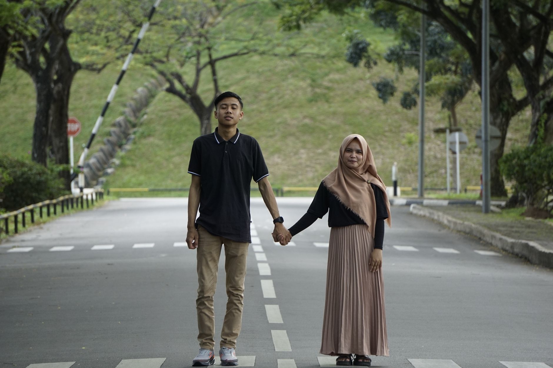 Seasang kekasih berjalan sambil bergandengan tangan di jalan berpaving yang dikelilingi pepohonan sebagai bukti cinta sejati.