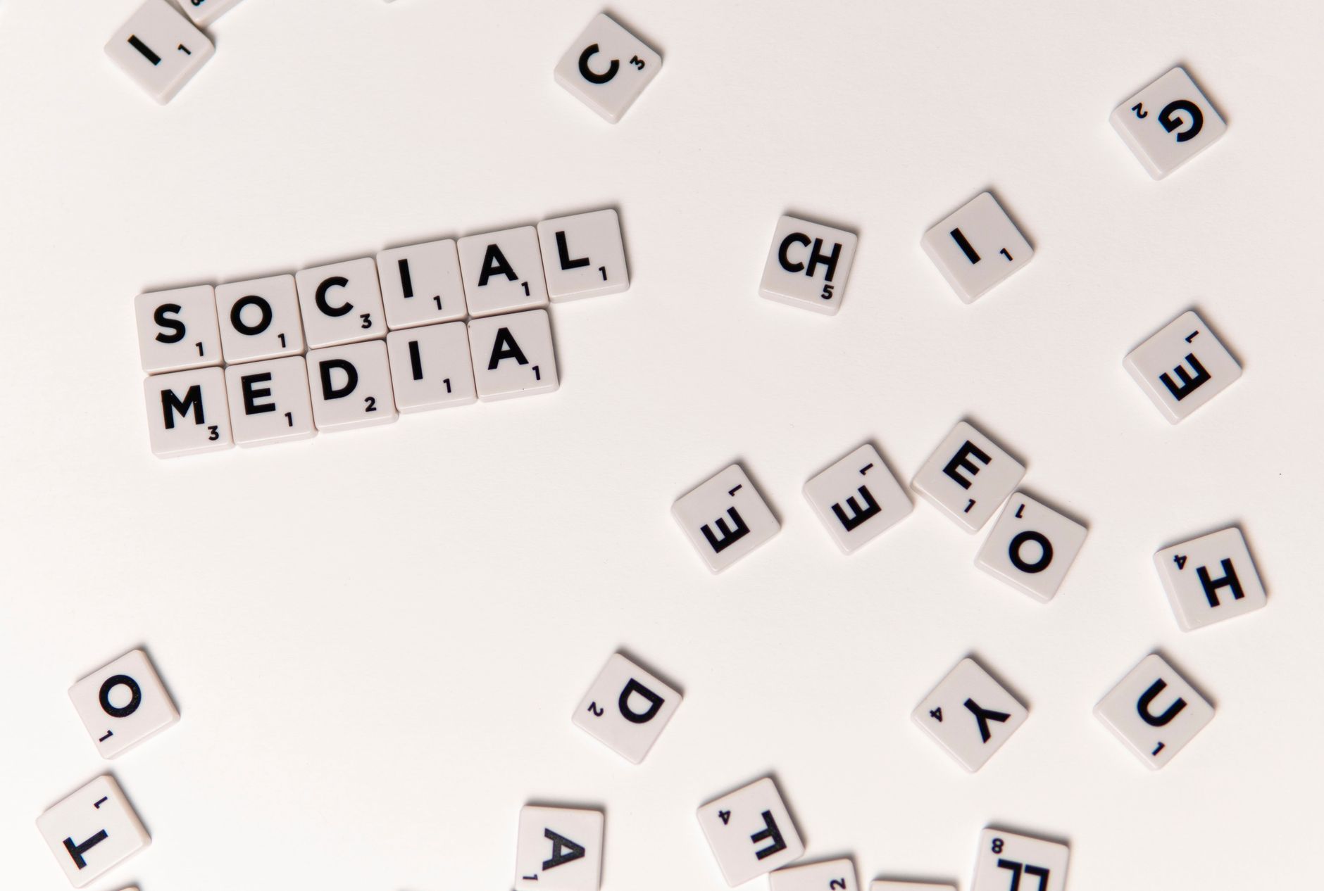 Scrabble tiles spelling "SOCIAL MEDIA" on a white background, surrounded by scattered letter tiles.