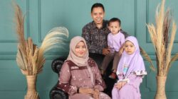 Keluarga berempat berpose bersama dengan latar belakang dinding biru dan tanaman kering.
