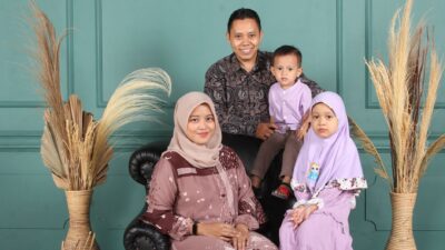 Keluarga berempat berpose bersama dengan latar belakang dinding biru dan tanaman kering.