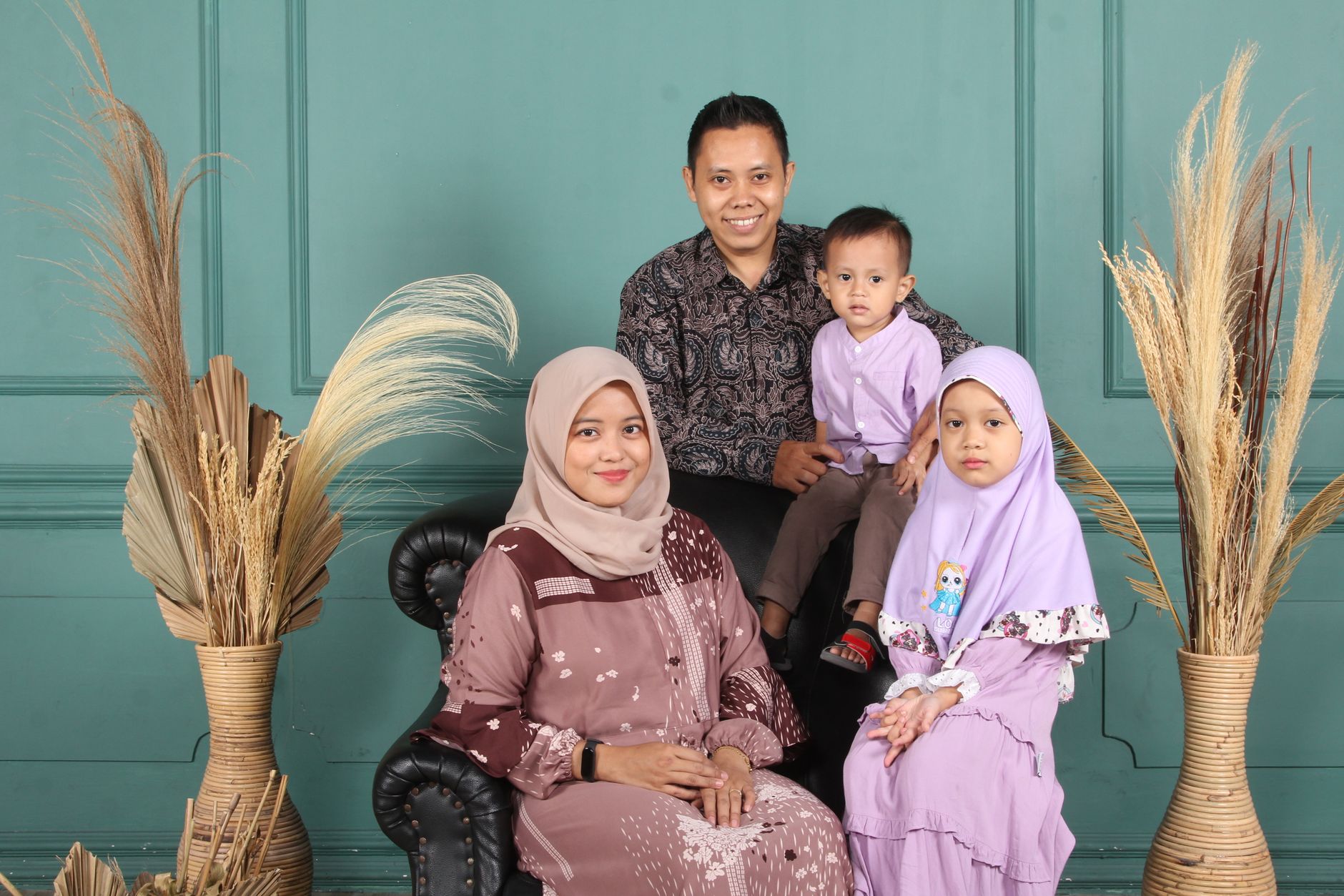 Keluarga berempat berpose bersama dengan latar belakang dinding biru dan tanaman kering.