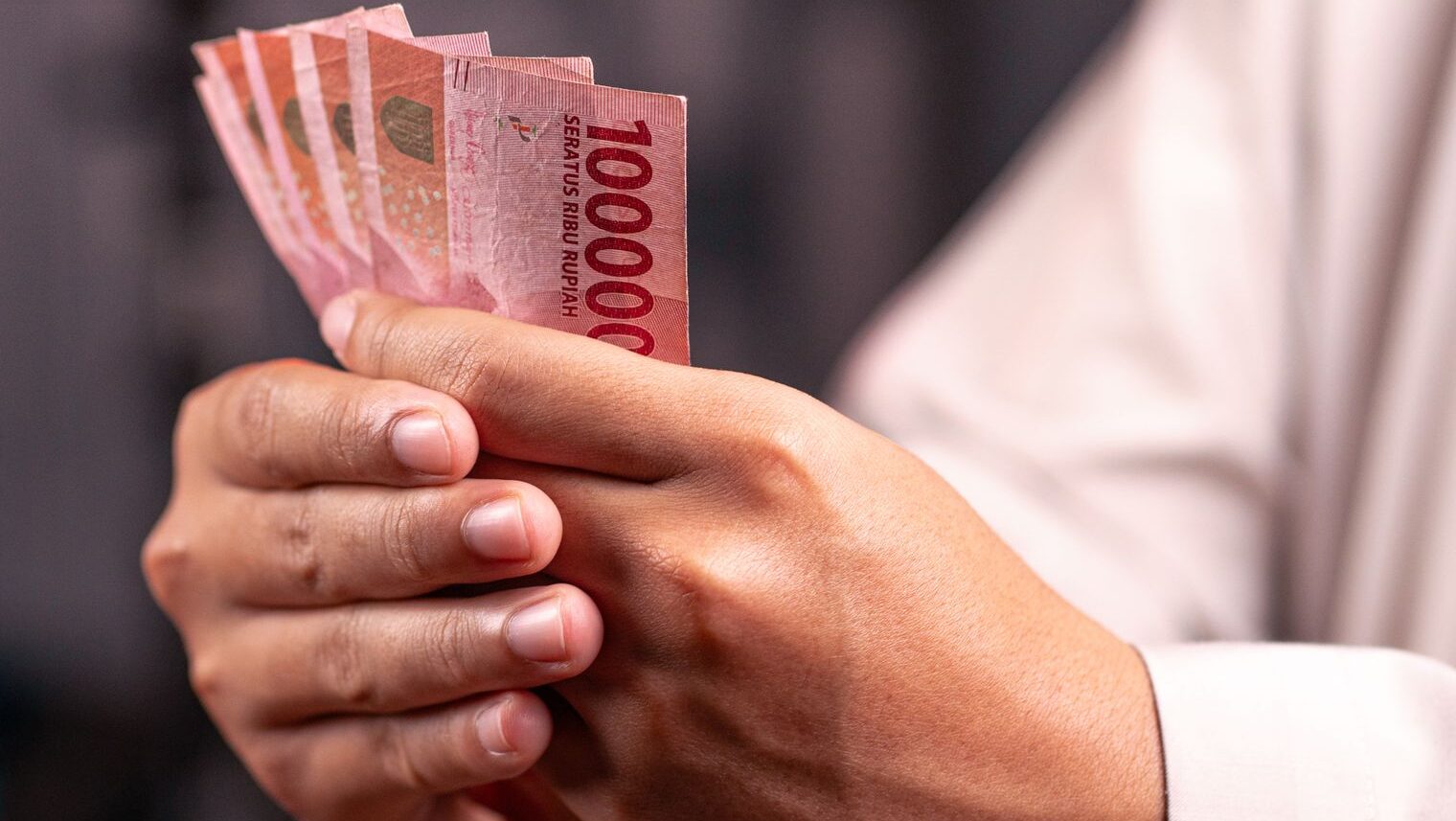 Seseorang memegang kipas uang kertas Rupiah untuk ilustrasi anggaran bulanan keuangan.