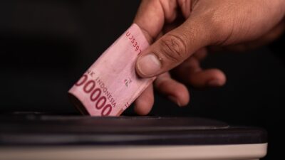 Tangan memasukkan uang rupiah ke dalam kotak sebagai ilustrasi menabung dana darurat.