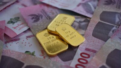 Three gold bars resting on a scattered pile of pink Indonesian rupiah banknotes.