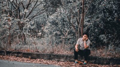 Young man sitting desolately on a roadside curb surrounded by autumn leaves, reflecting on the benefits of being single.