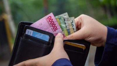 Seseorang mengeluarkan uang Rupiah dari dompet kulit hitam berisi kartu kredit.