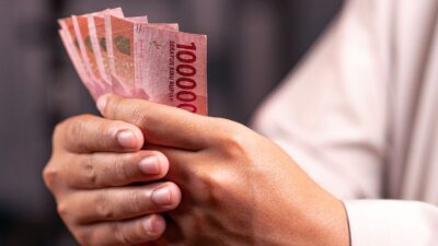 Seseorang memegang dan menghitung uang kertas Rupiah untuk panduan investasi pemula.