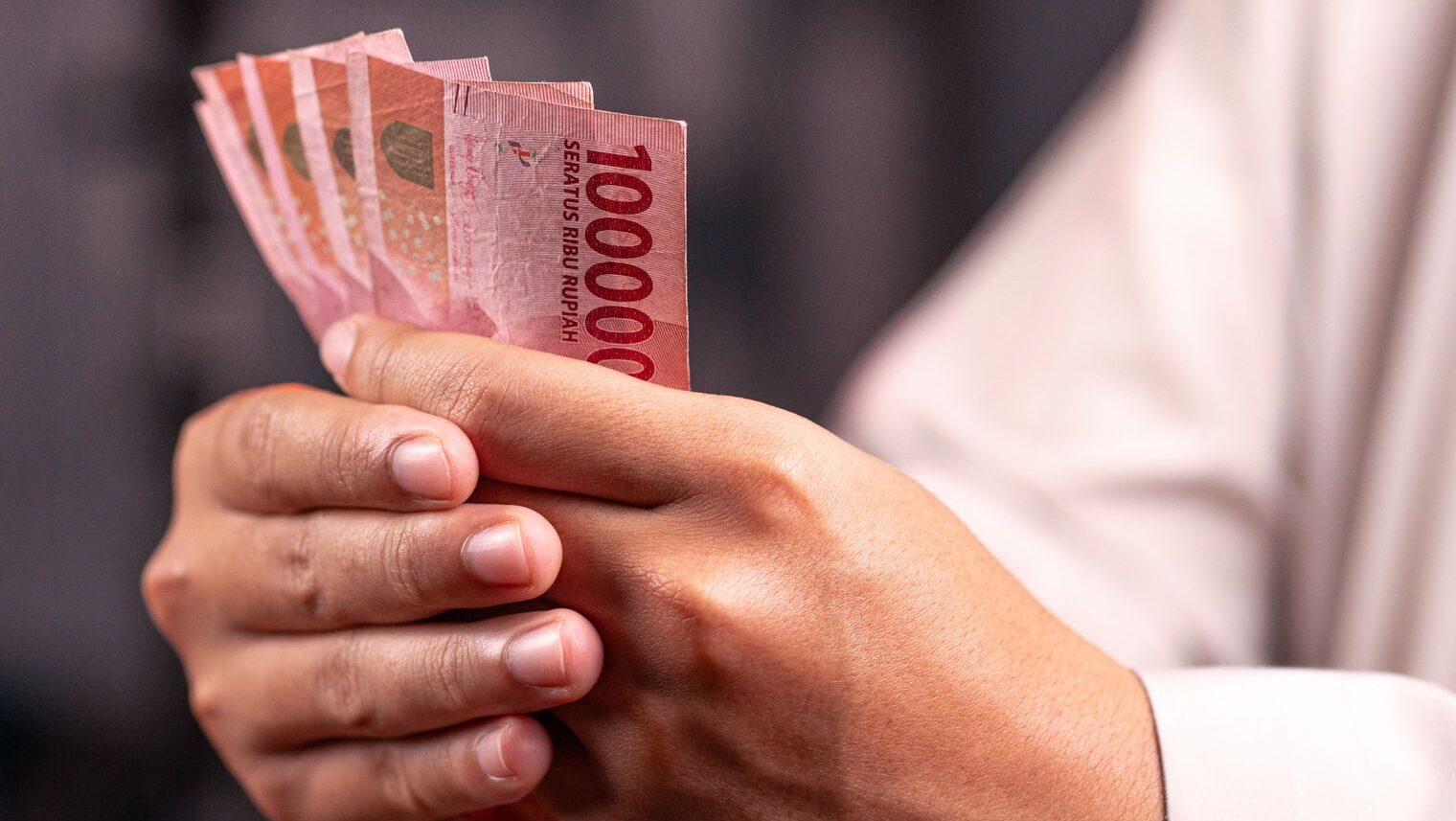 Seseorang memegang uang kertas Rupiah sebagai simbol pertumbuhan kekayaan finansial.