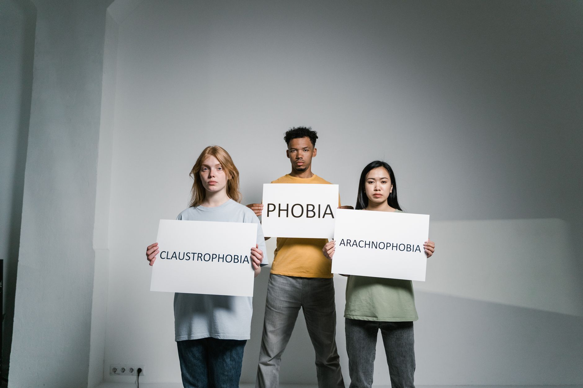 Three diverse people holding signs about phobias, representing Fobia Sosial.