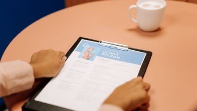 Hands reviewing a CV lolos ATS on a clipboard at a table with coffee.