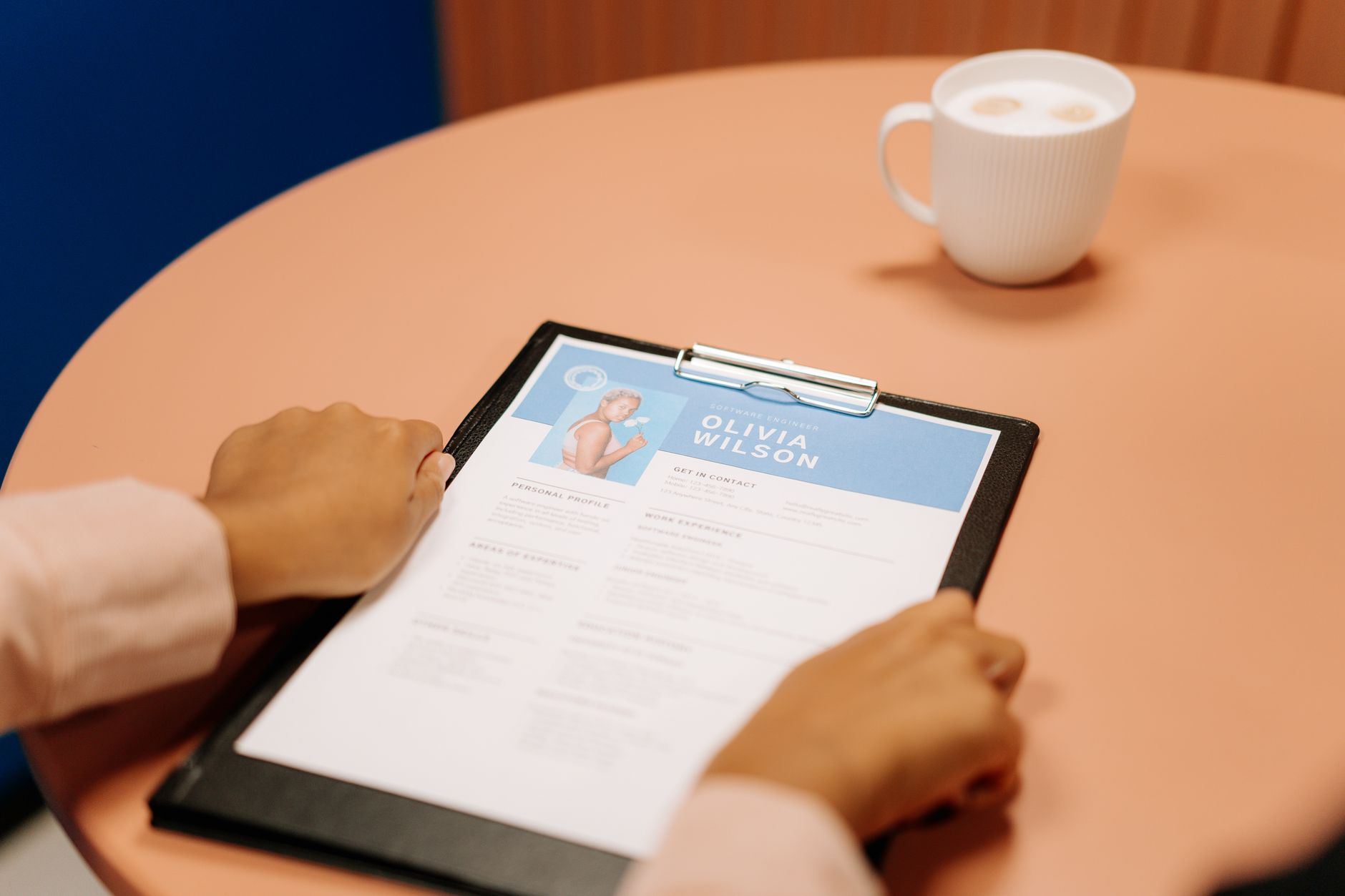 Hands reviewing a CV lolos ATS on a clipboard at a table with coffee.