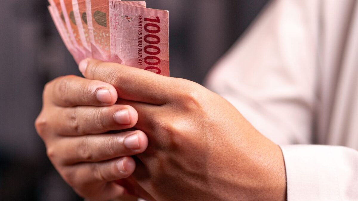 Seseorang menghitung uang kertas pecahan seratus ribu rupiah sebagai Indikator Keuangan Aman.