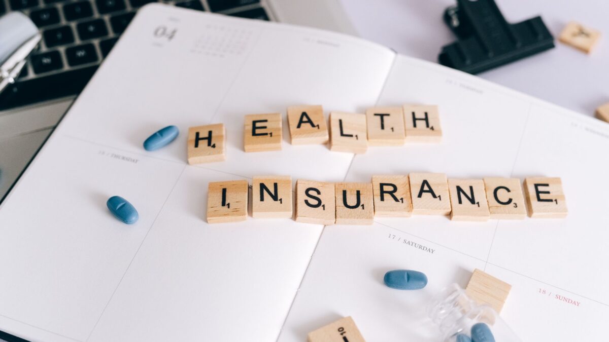 Wooden letter tiles spelling health insurance on a calendar with blue pills.