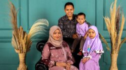 Happy family of four smiling together in a studio with a teal wall and pampas grass.