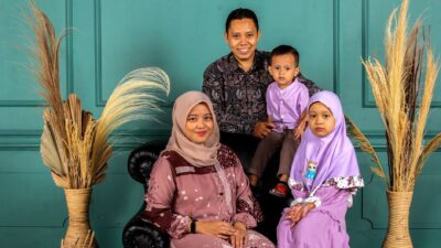 Happy family of four smiling together in a studio with a teal wall and pampas grass.