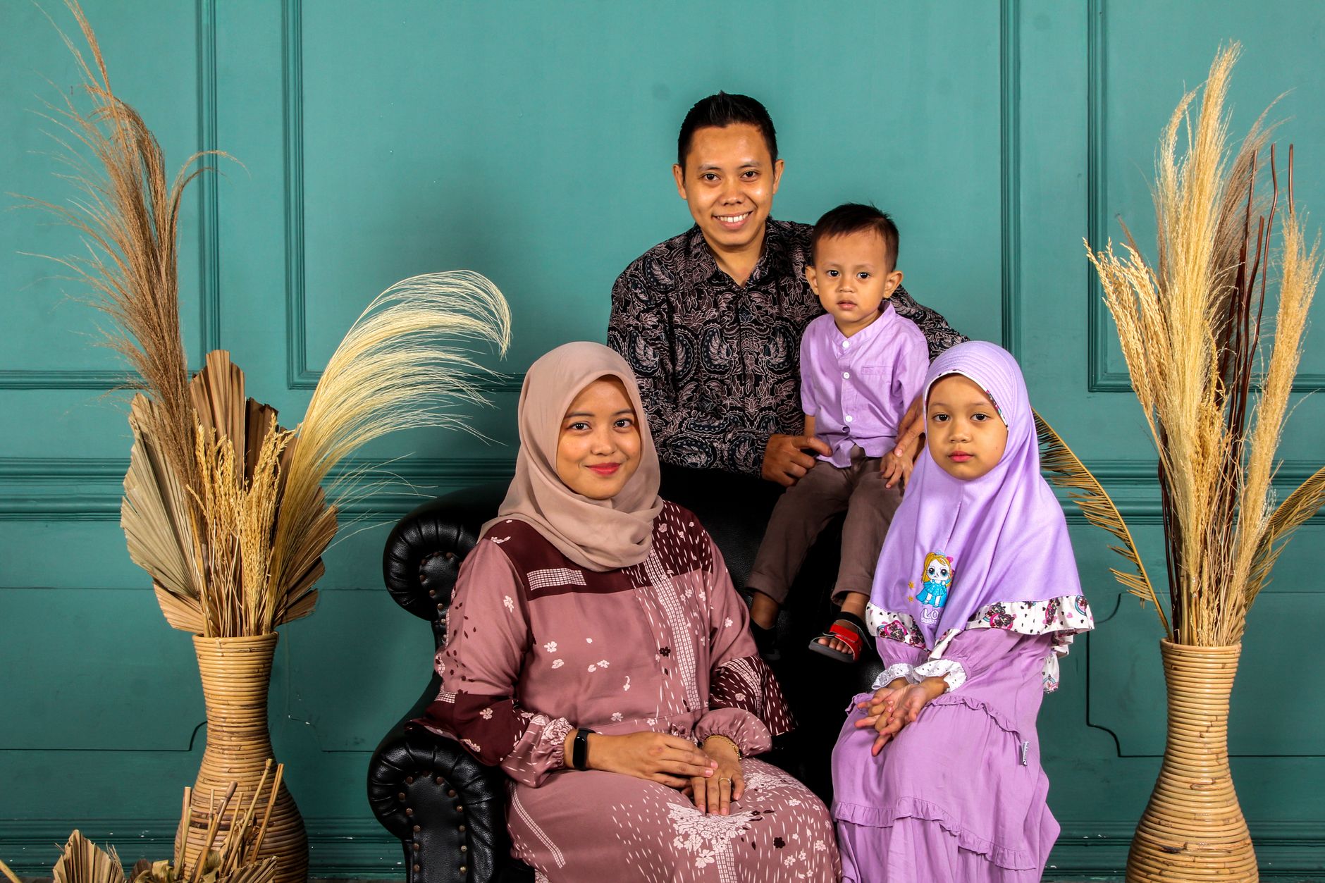 Happy family of four smiling together in a studio with a teal wall and pampas grass.