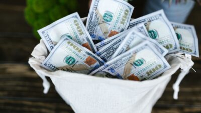 A drawstring pouch filled with US hundred dollar bills on a wooden table.