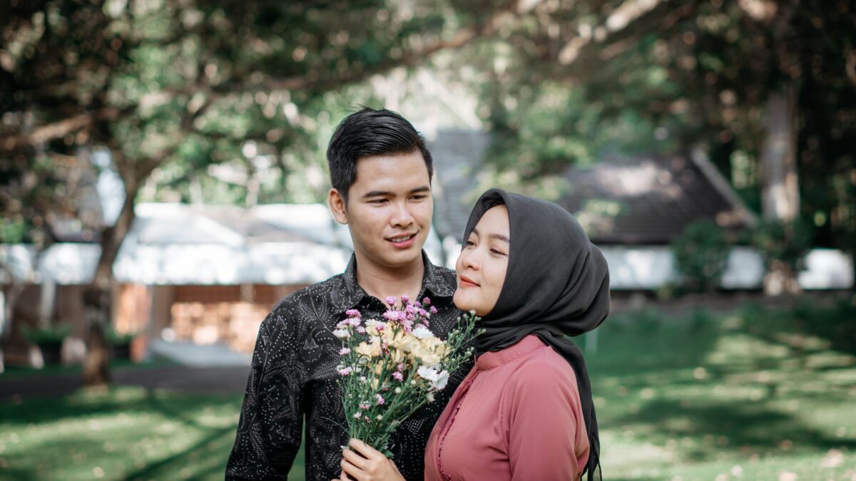 Pria tulus mencintai dan wanita berhijab memegang buket bunga di luar ruangan.