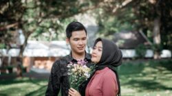 Pria tulus mencintai dan wanita berhijab memegang buket bunga di luar ruangan.