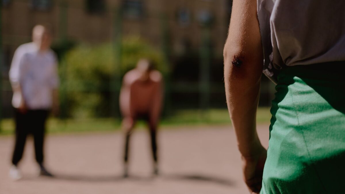 A close-up of a person's scraped elbow on an outdoor court, related to Mother Wound Psikologis.