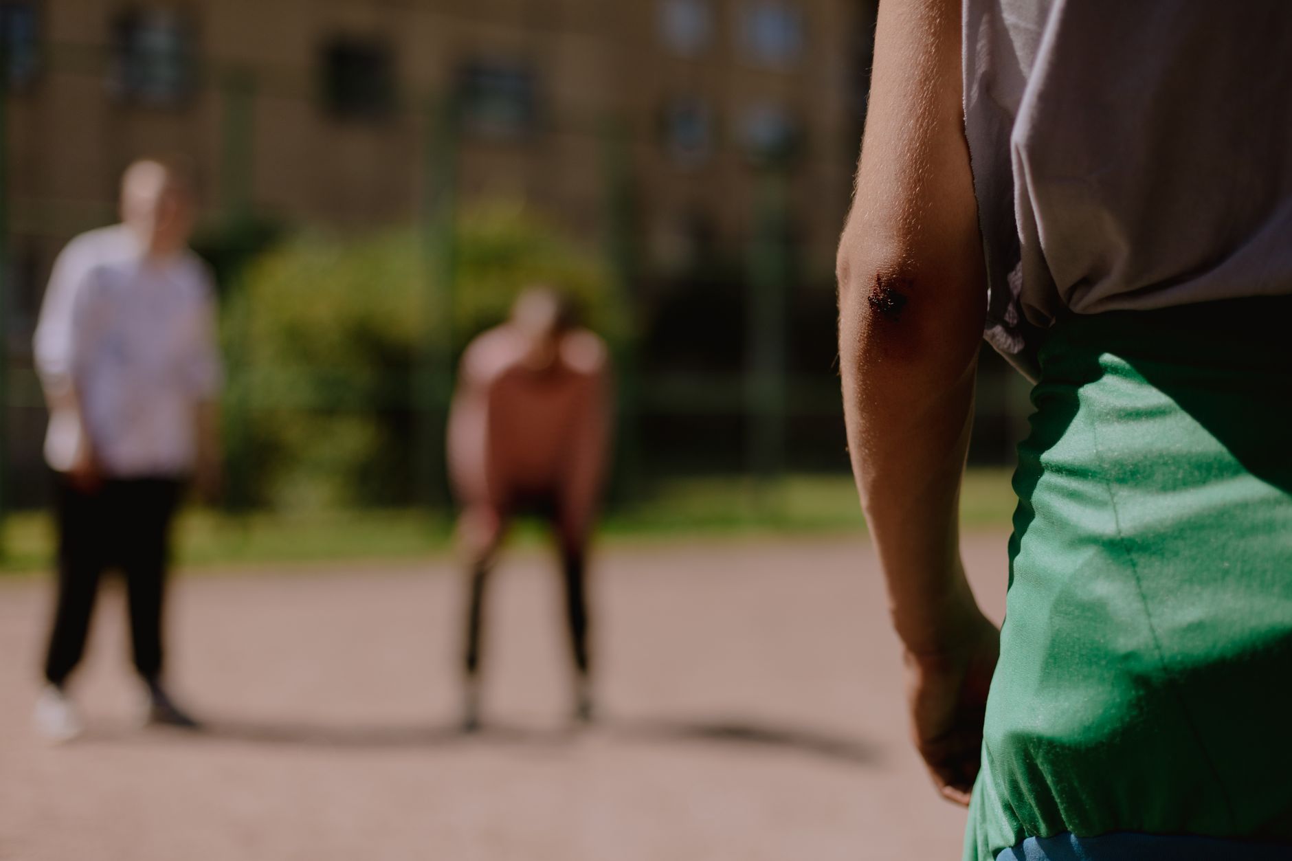 A close-up of a person's scraped elbow on an outdoor court, related to Mother Wound Psikologis.