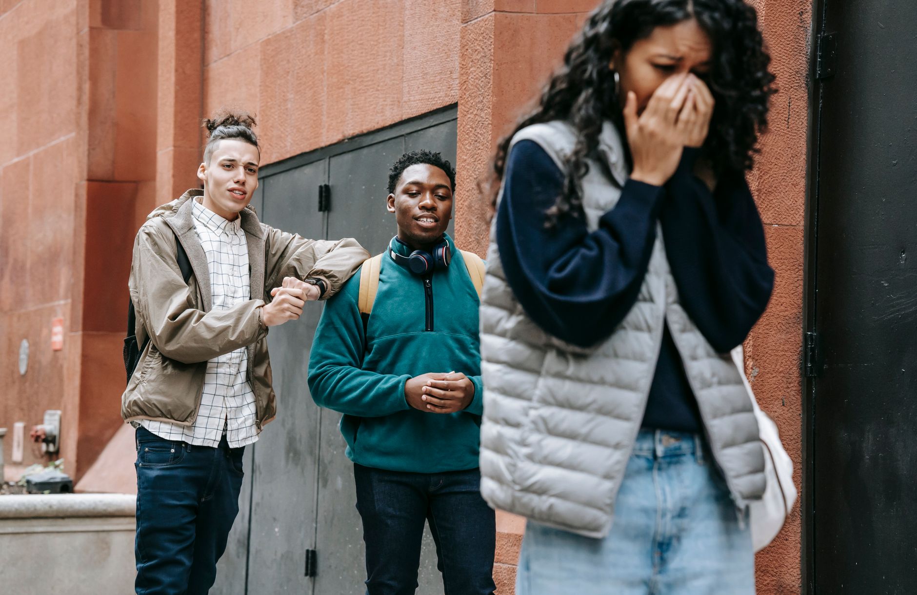 Two boys laughing and pointing at a distressed teenage girl covering her face, depicting peer bullying.