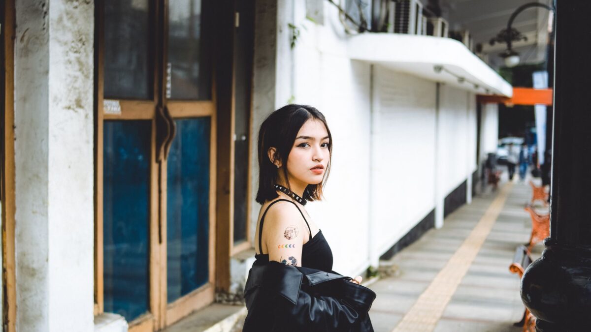 Stylish woman in a black top and leather jacket walking on an urban sidewalk, showcasing a trendy gaya rambut wanita.