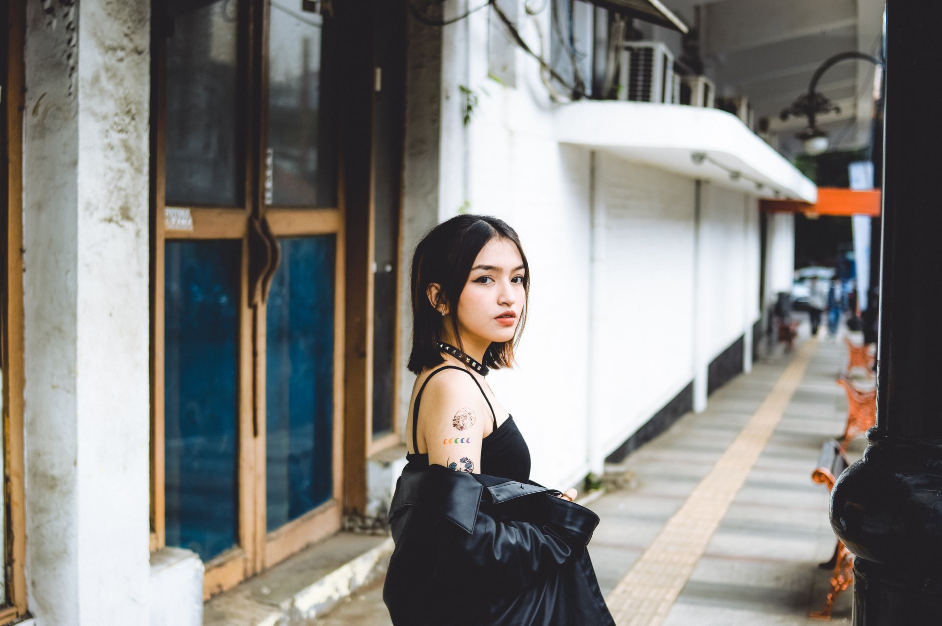 Stylish woman in a black top and leather jacket walking on an urban sidewalk, showcasing a trendy gaya rambut wanita.