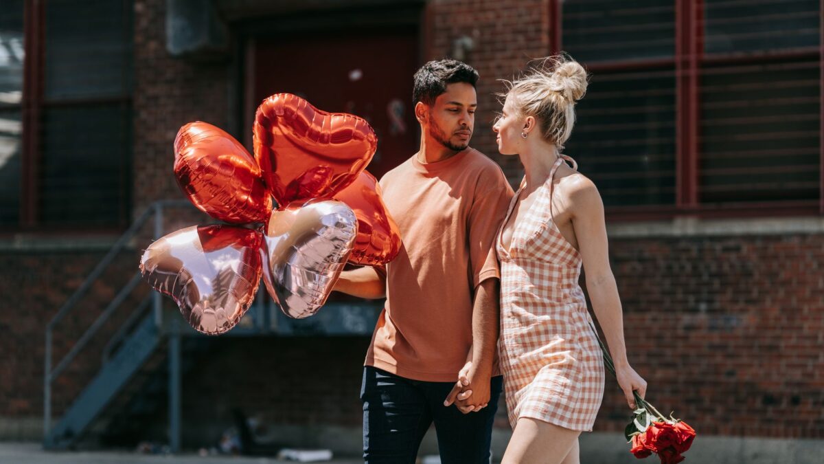Pasangan muda berjalan membawa balon hati, ilustrasi Perbedaan Infatuation Cinta untuk memilih pasangan.