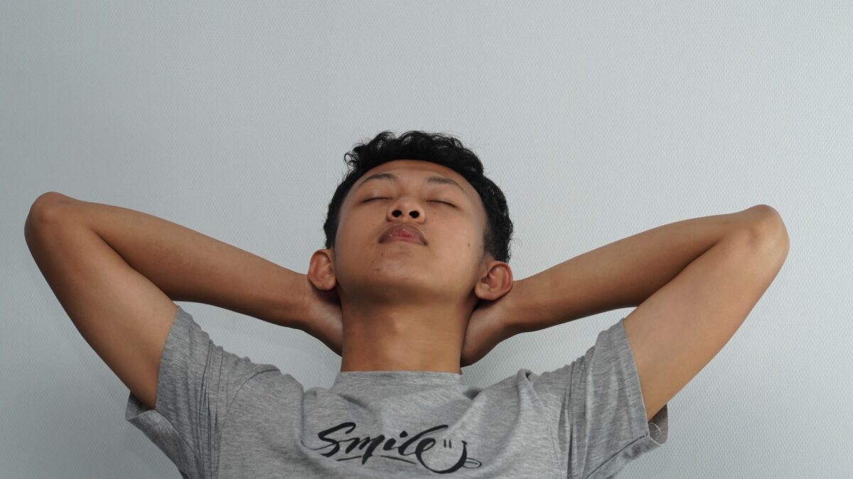 Seorang pria tersenyum santai dengan mata tertutup dan tangan di belakang kepala, menunjukkan Pria Nyaman Emosional.