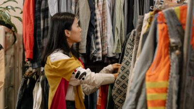 Seorang wanita sedang memilih pakaian dari rak untuk memulai bisnis thrift di rumah.
