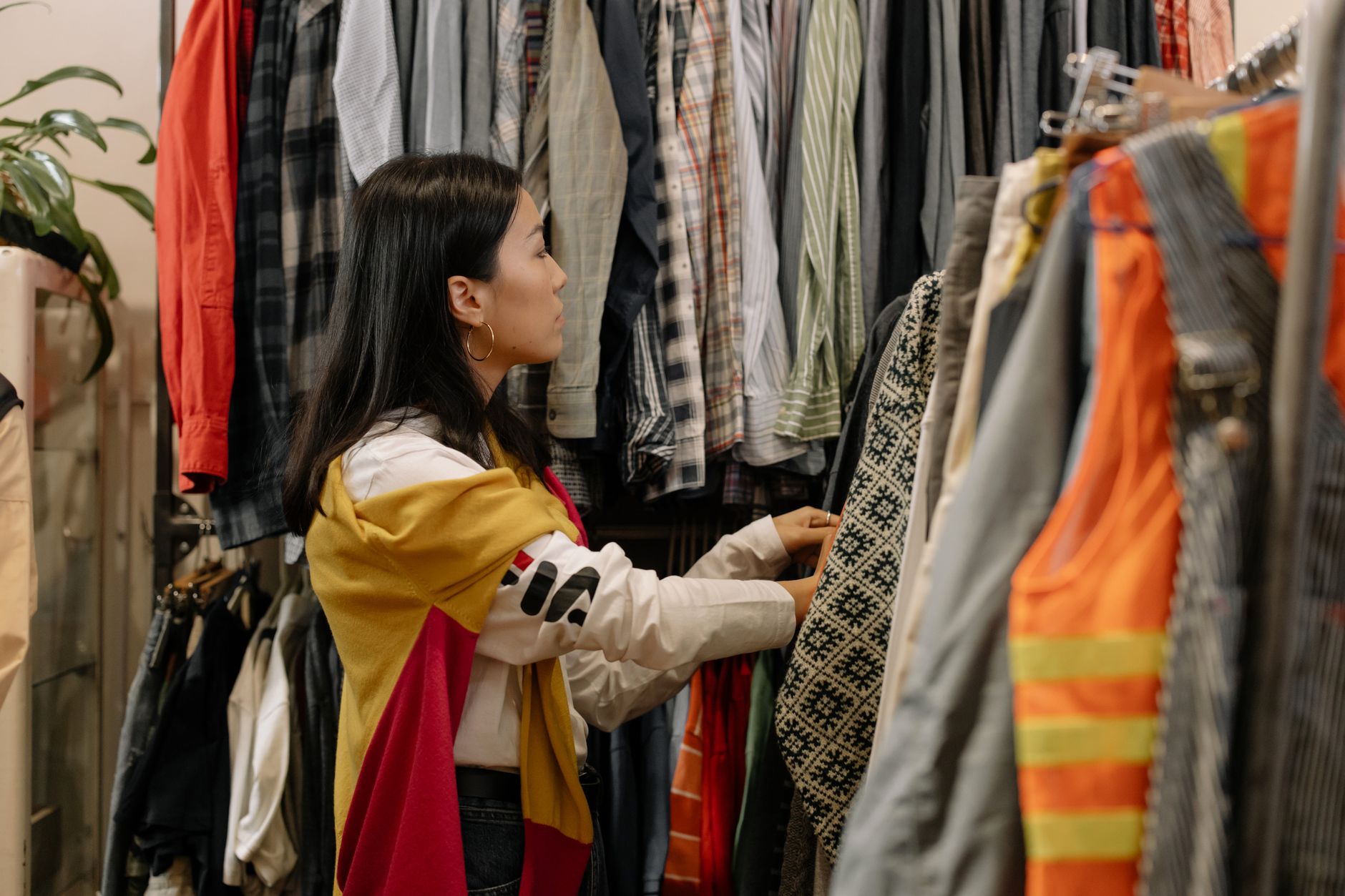 Seorang wanita sedang memilih pakaian dari rak untuk memulai bisnis thrift di rumah.