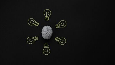 A central human brain model surrounded by glowing lightbulb outlines on a black surface.