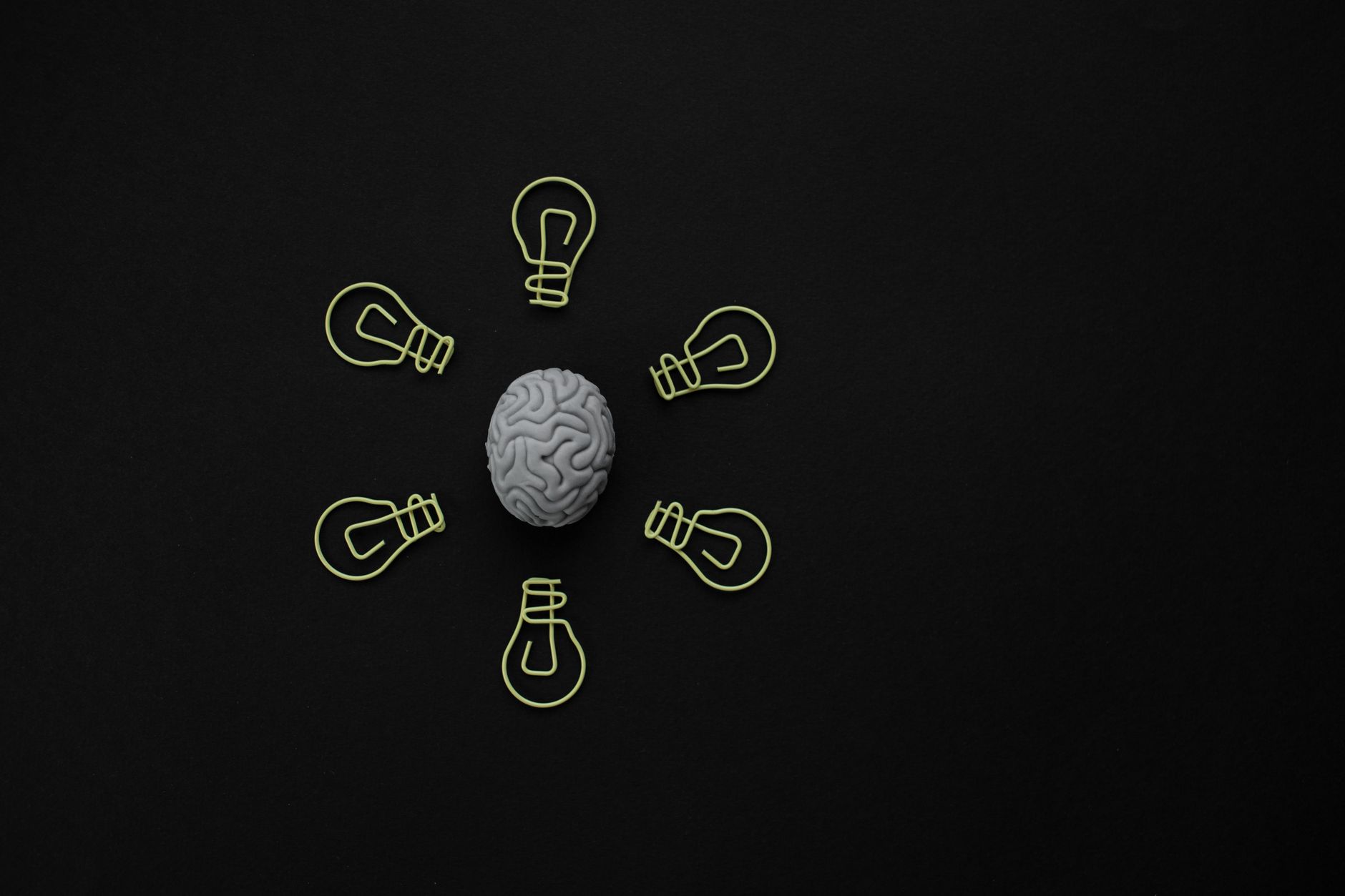 A central human brain model surrounded by glowing lightbulb outlines on a black surface.